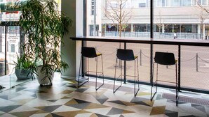 A modern interior with a geometric patterned floor, a large potted plant, and a view of a cityscape through large windows. - ibis Kaunas Centre (Kaunas)