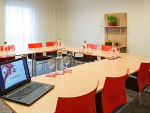 A conference room with a laptop, red chairs, a long table, and a potted plant on a shelf. - ibis Kaunas Centre (Kaunas)