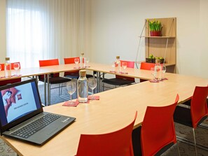 A conference room with a laptop, red chairs, a long table, and a potted plant on a shelf. - ibis Kaunas Centre (Kaunas)