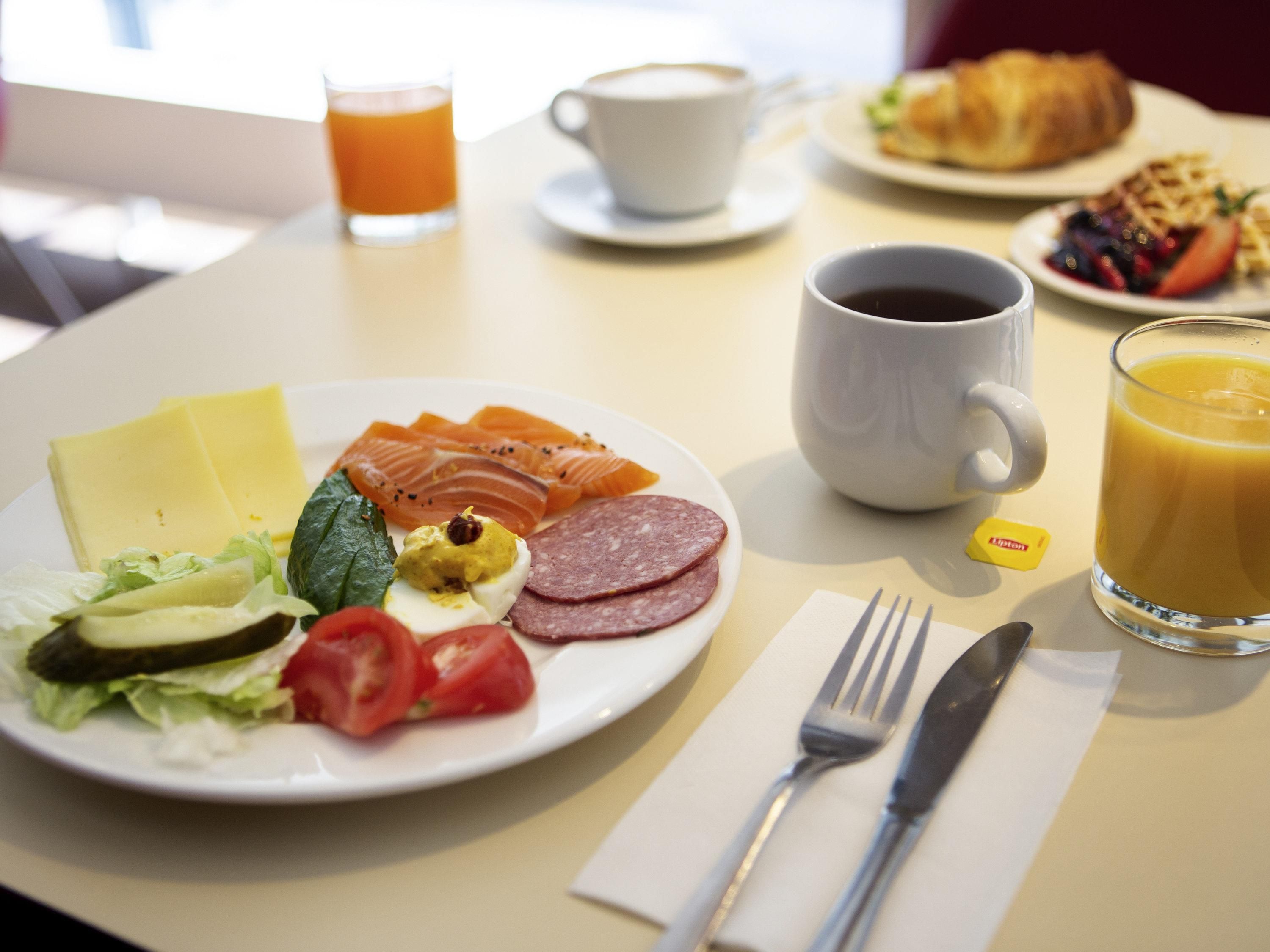 Ein Frühstückstisch mit Teller, Tasse Kaffee, Glas Orangensaft und einem Croissant.