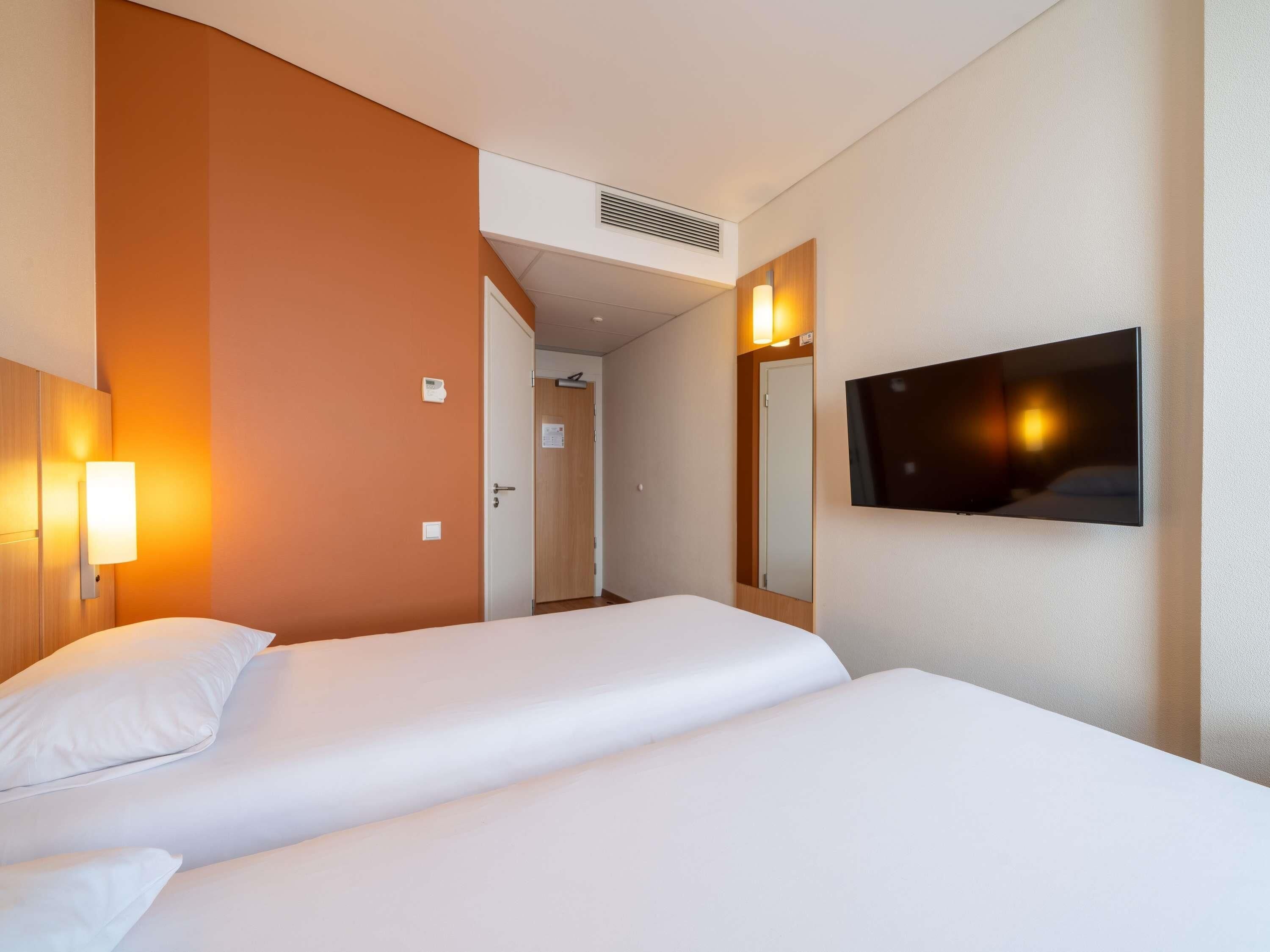 A hotel room with two beds, a TV, and a door leading to another room.