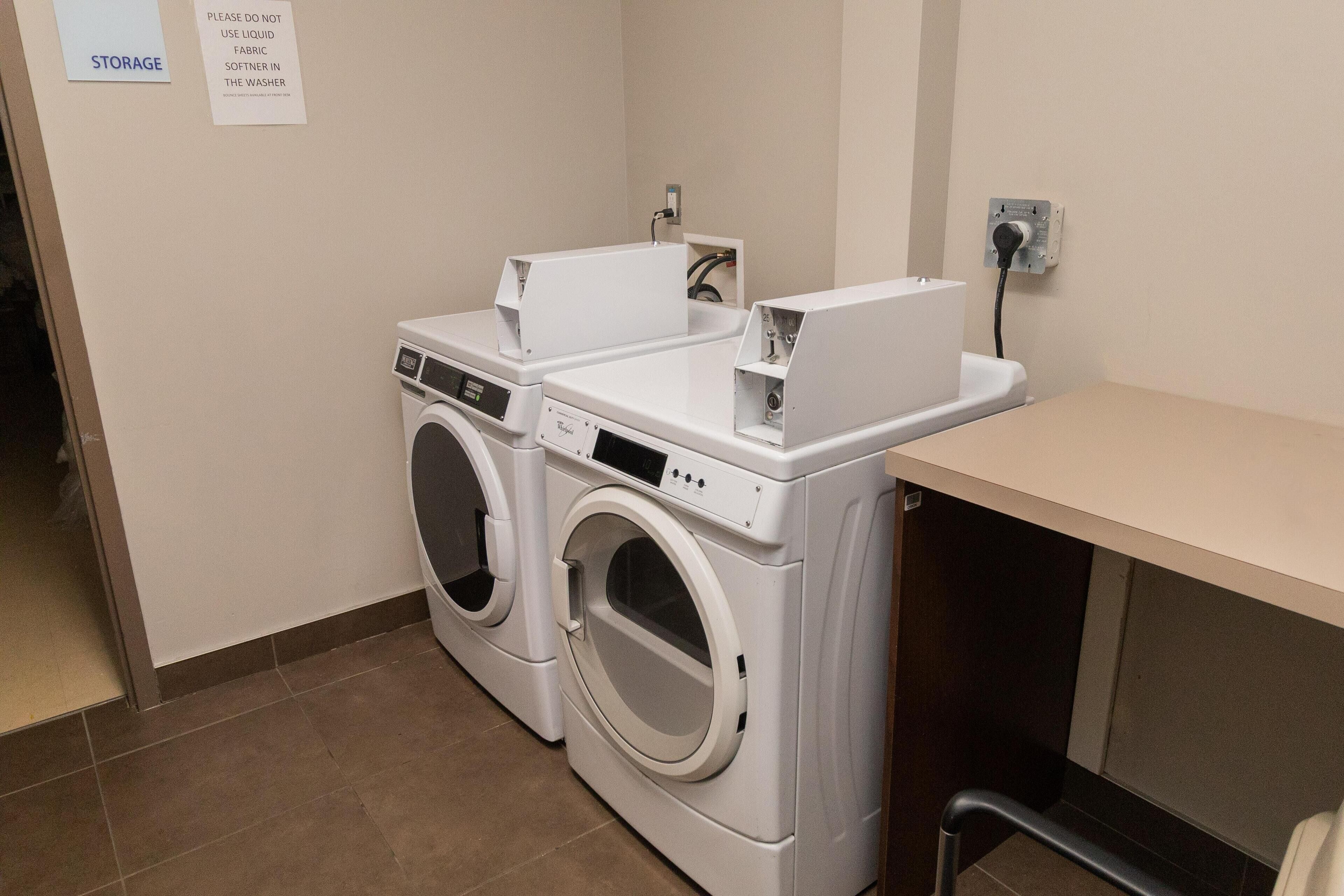 A laundry area with two front-loading washing machines, a storage sign, and a caution sign advising against using liquid fabric softener in the washer.