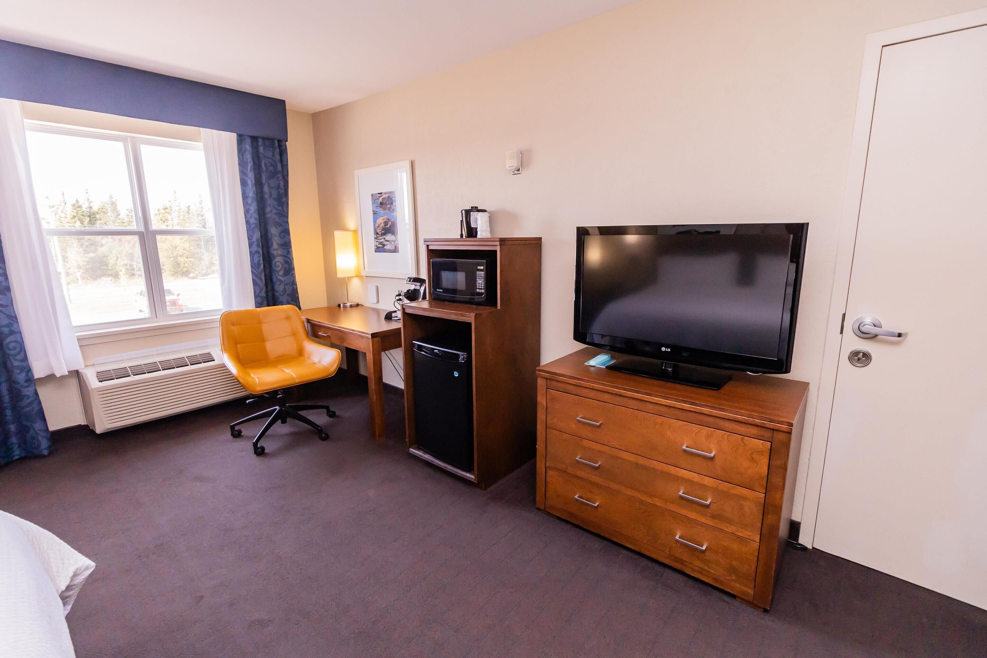 Une chambre d’hôtel équipée d’un lit, d’un bureau avec un ordinateur, d’une télévision, d’un four à micro-ondes et d’un petit réfrigérateur.