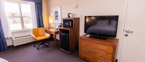 Une chambre d’hôtel équipée d’un lit, d’un bureau avec un ordinateur, d’une télévision, d’un four à micro-ondes et d’un petit réfrigérateur.