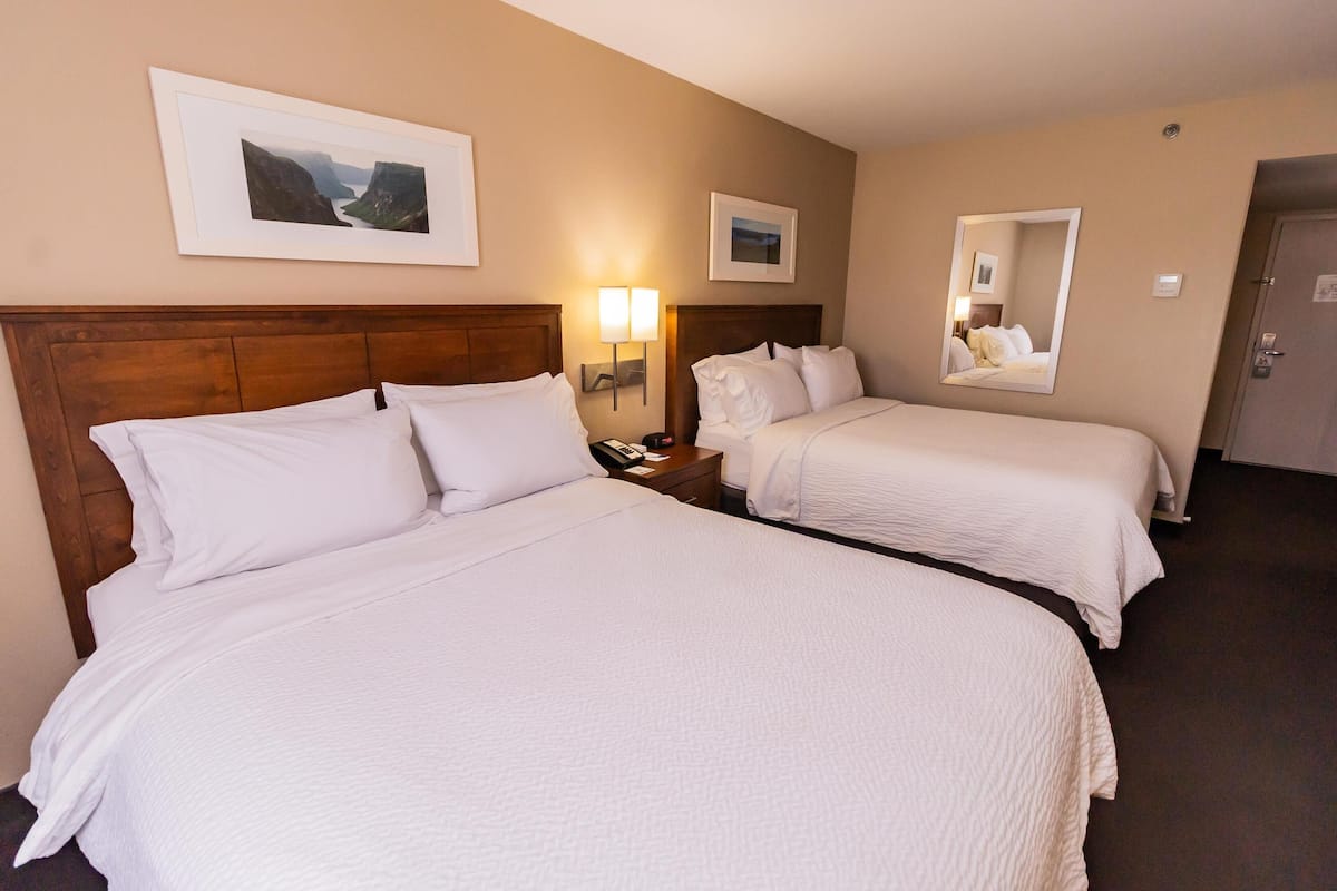 A hotel room with two beds, a wooden headboard, a nightstand with a lamp, and framed pictures on the wall.