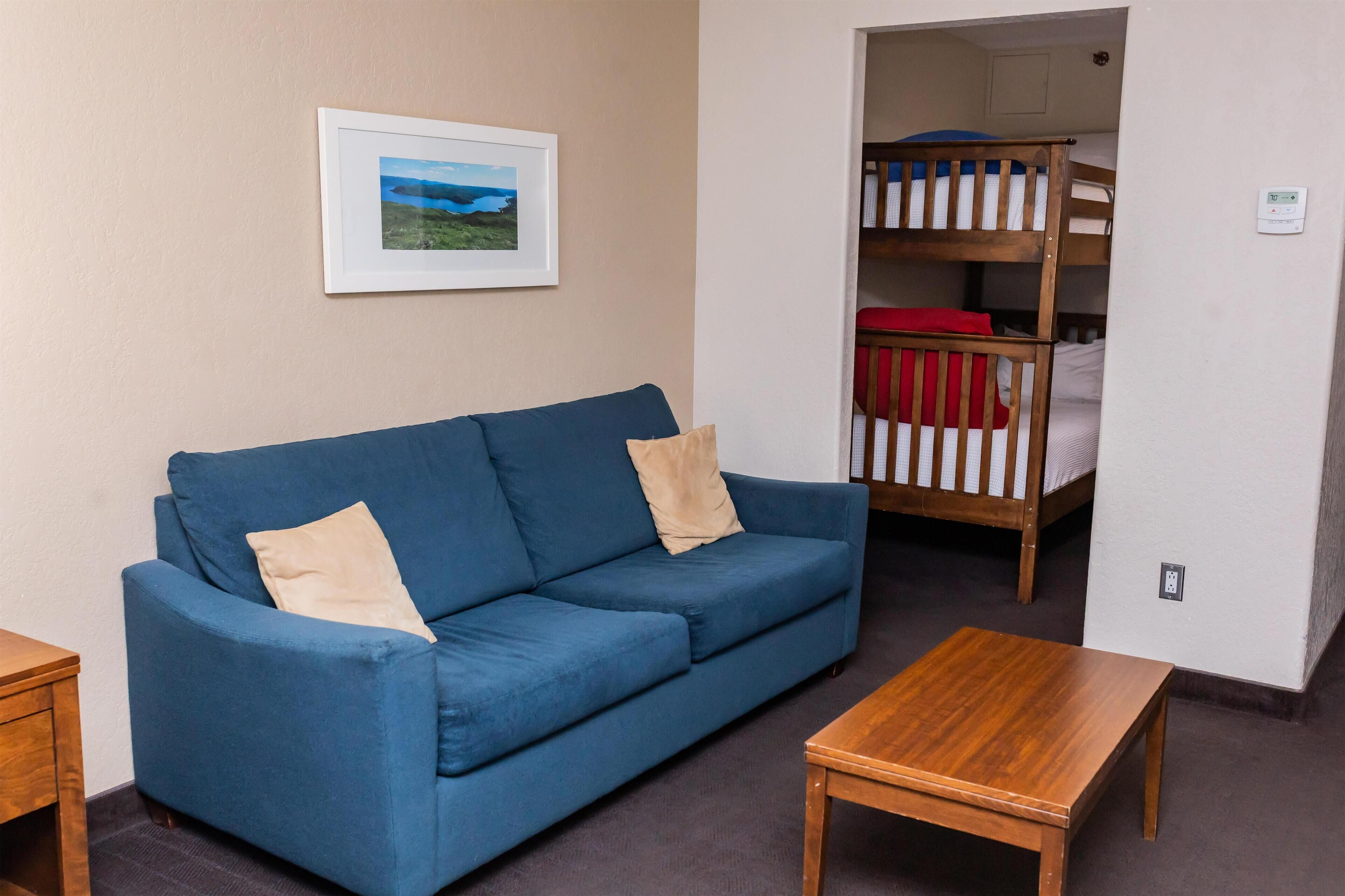 A room with a blue sofa, a wooden table, and a bunk bed with red bedding.