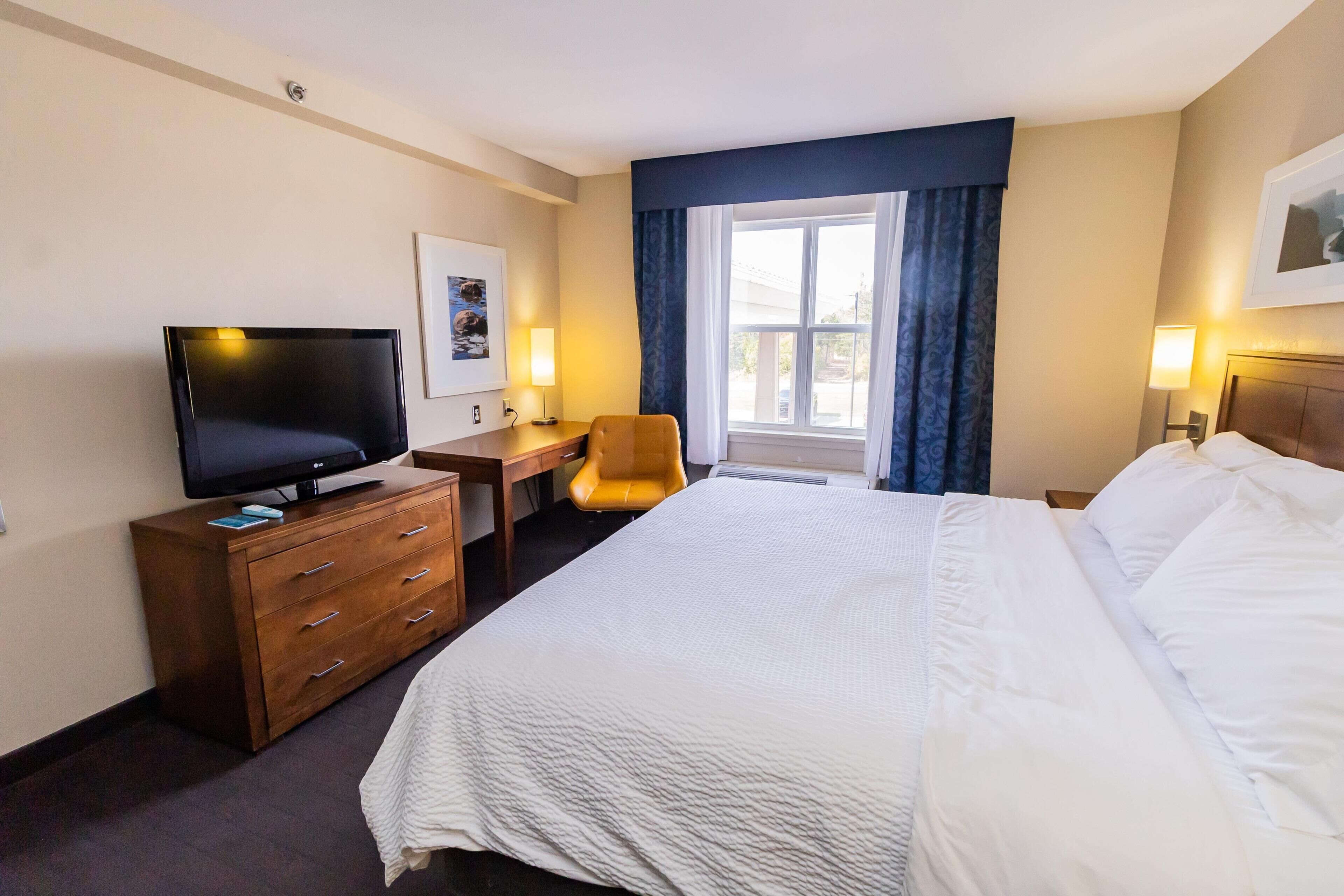 A hotel room with a large bed, a desk with a chair, a television, and a window with curtains.