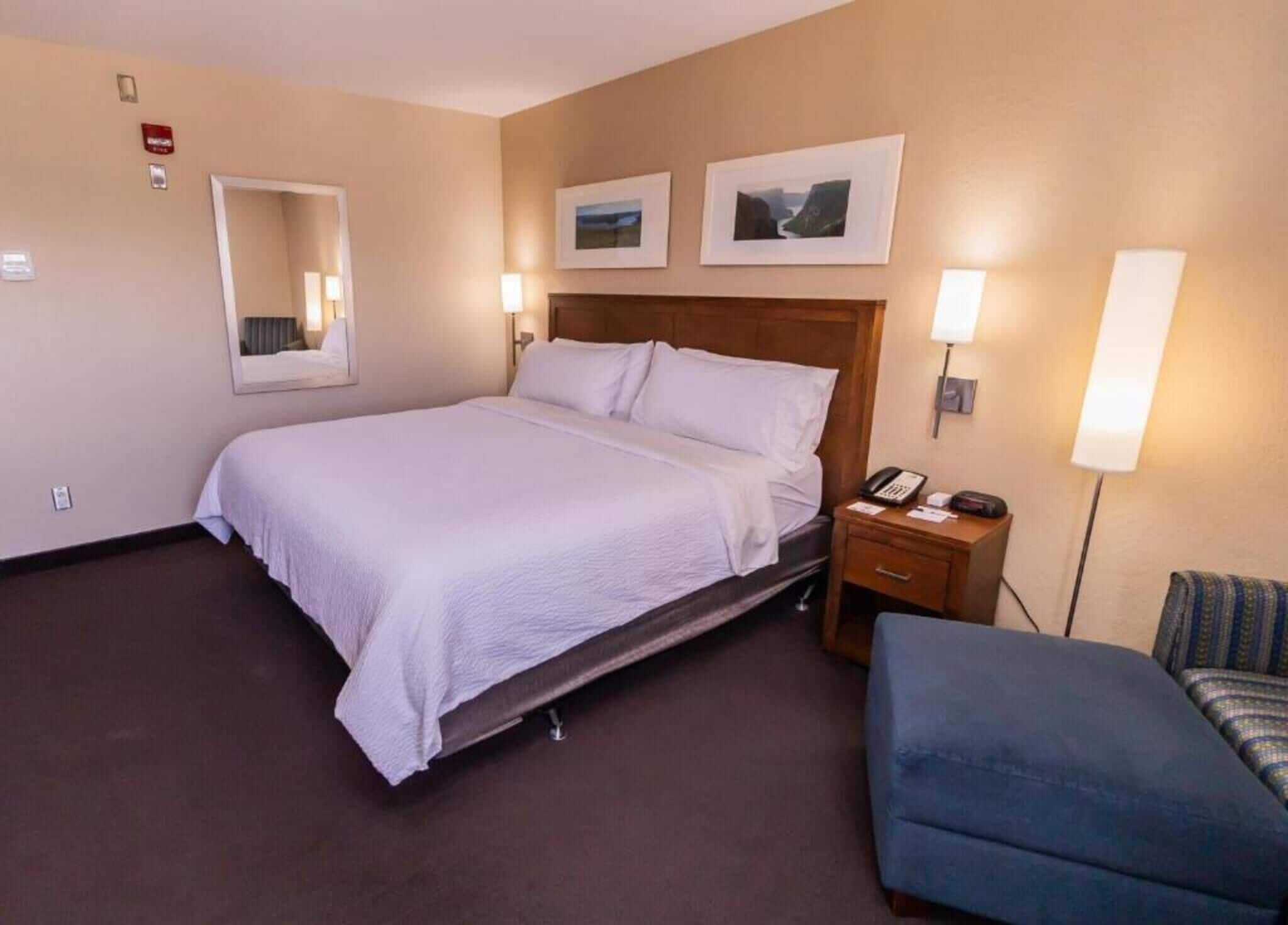 A hotel room with a bed, bedside table, lamp, chair, and two framed pictures on the wall.