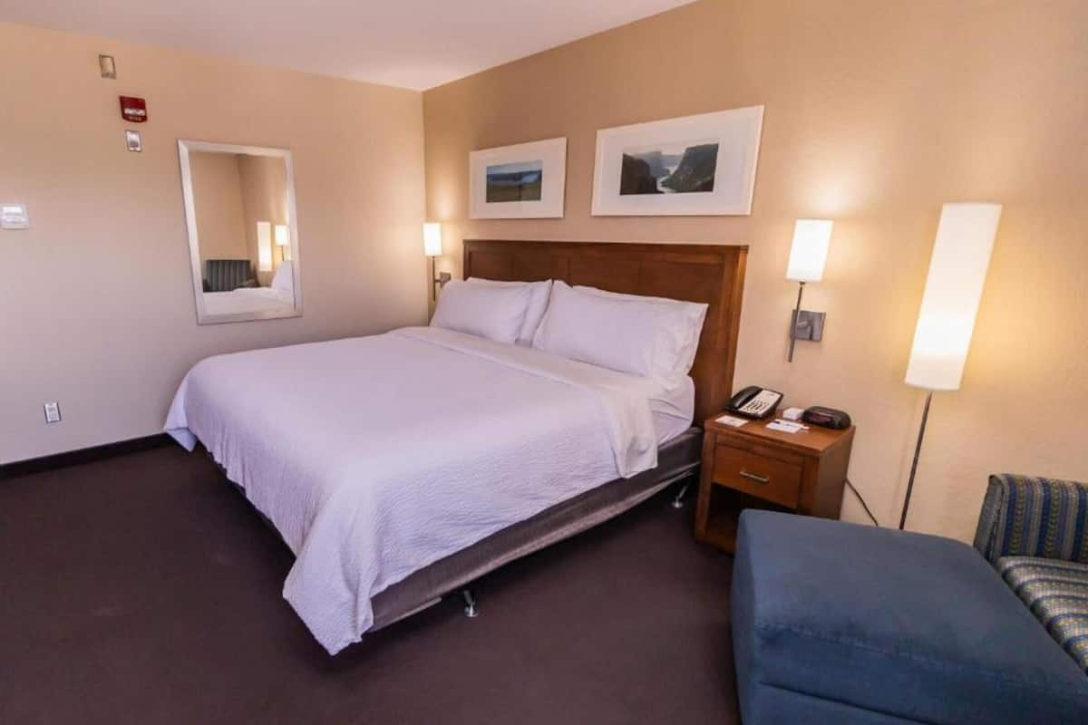 A hotel room with a bed, bedside table, lamp, chair, and two framed pictures on the wall.