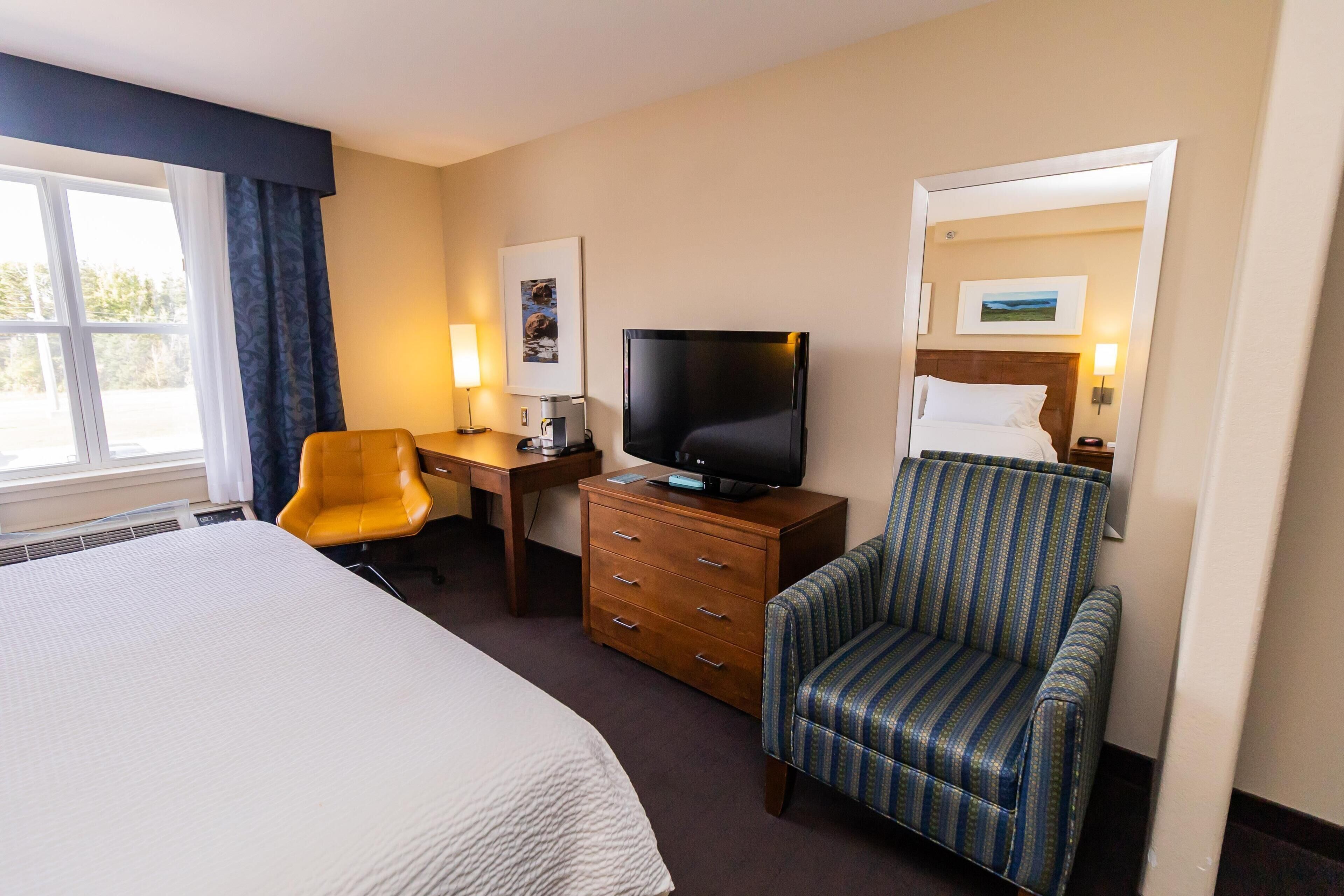 A hotel room with a large bed, a desk with a television, a chair, and a sofa.
