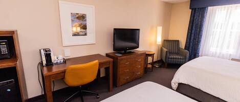 A hotel room with a bed, a desk with a chair, a television, a coffee maker, and a framed picture on the wall.