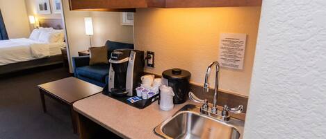 A hotel room with a kitchenette, including a coffee maker, a sink, and a microwave.