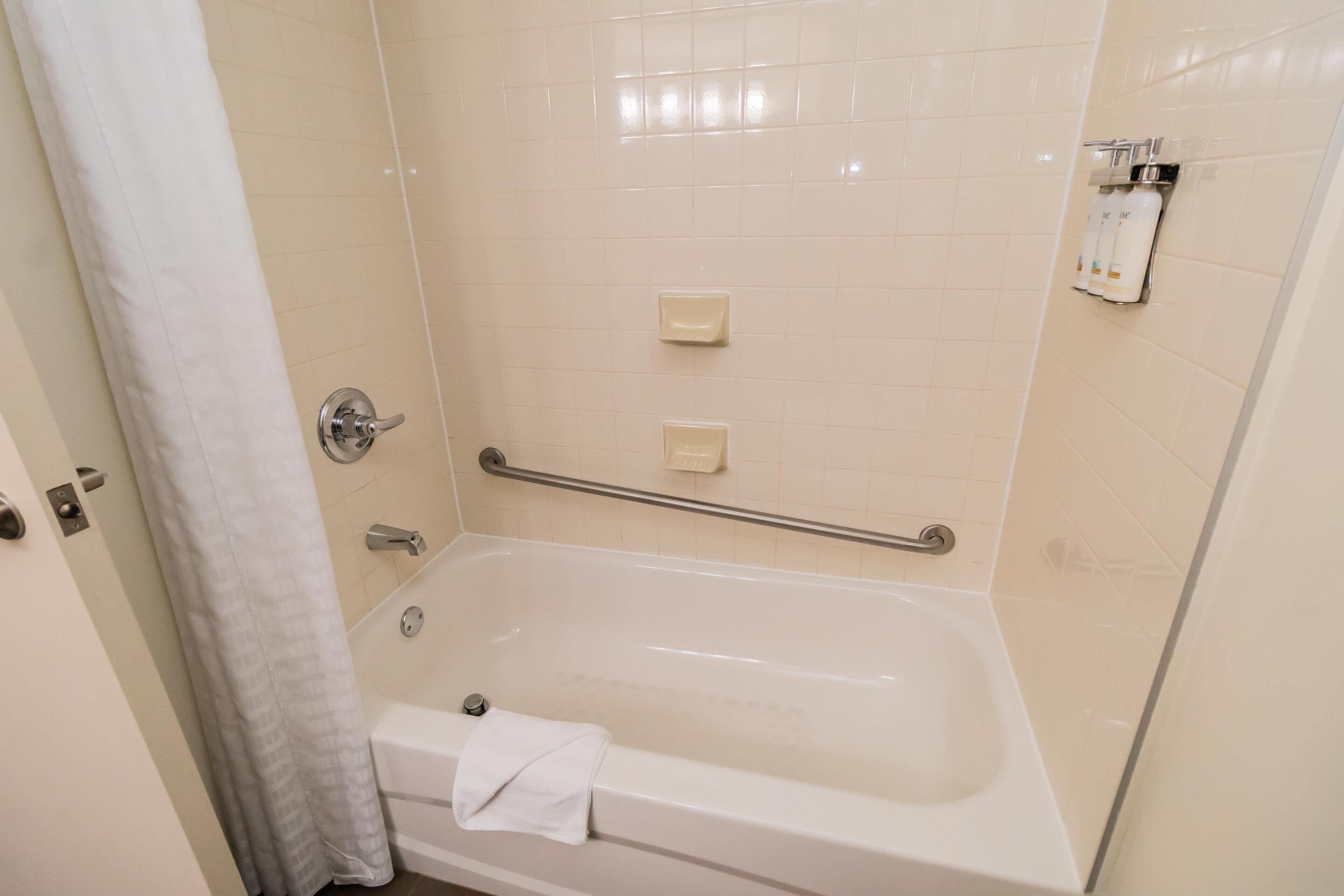 A bathroom with a bathtub, a shower curtain, a handrail, and a towel rack.