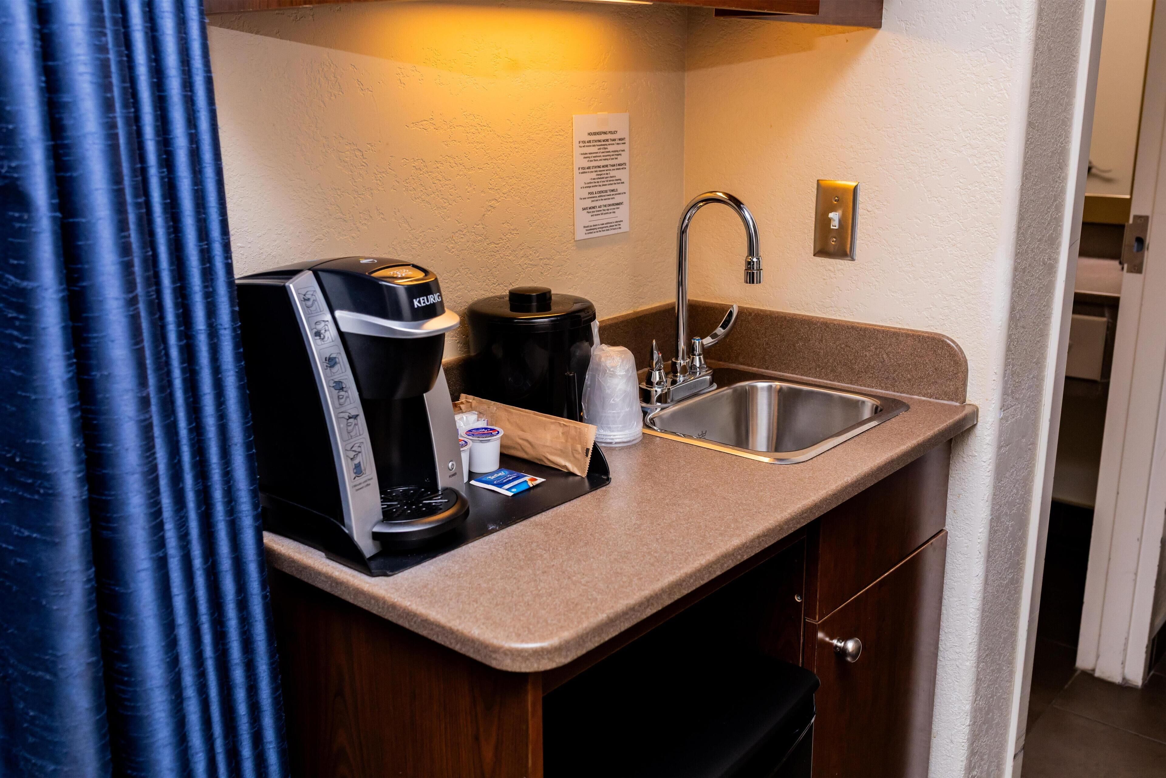A kitchenette with a coffee maker, a kettle, a sink, and a countertop.