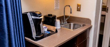 A kitchenette with a coffee maker, a kettle, a sink, and a countertop.