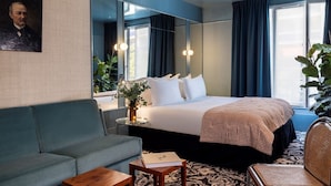 A hotel room with a bed, a sofa, a small table, a mirror, and a large window with curtains. - La Conversation (Paris)