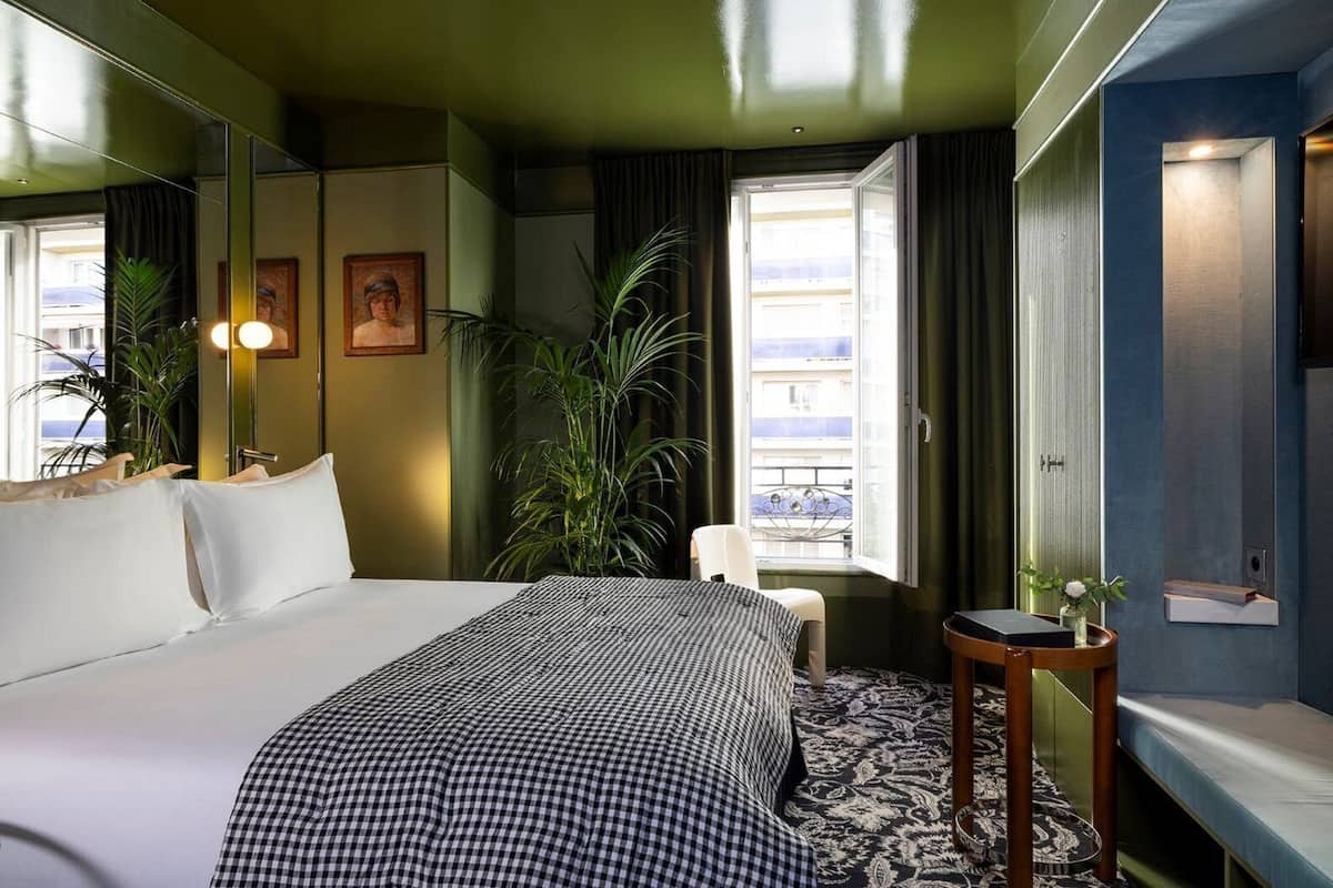 A hotel room with a large bed, a chair, a small table, and a window with curtains.