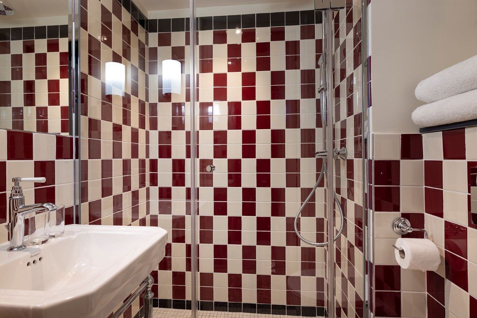 A bathroom with a checkered tile pattern, a glass shower enclosure, a sink, and a towel rack.
