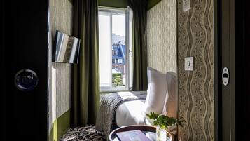 Hotelkamer met een bed, een nachtkastje met een boek en een vaas, een raam met gordijnen, en behang met een patroon.