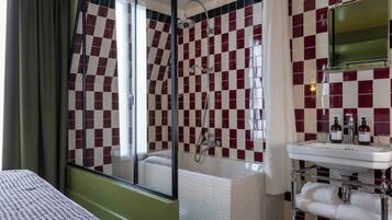 Une salle de bain avec un mur recouvert de carreaux à motifs, une baignoire, une douche, un lavabo avec des articles de toilette et un miroir.