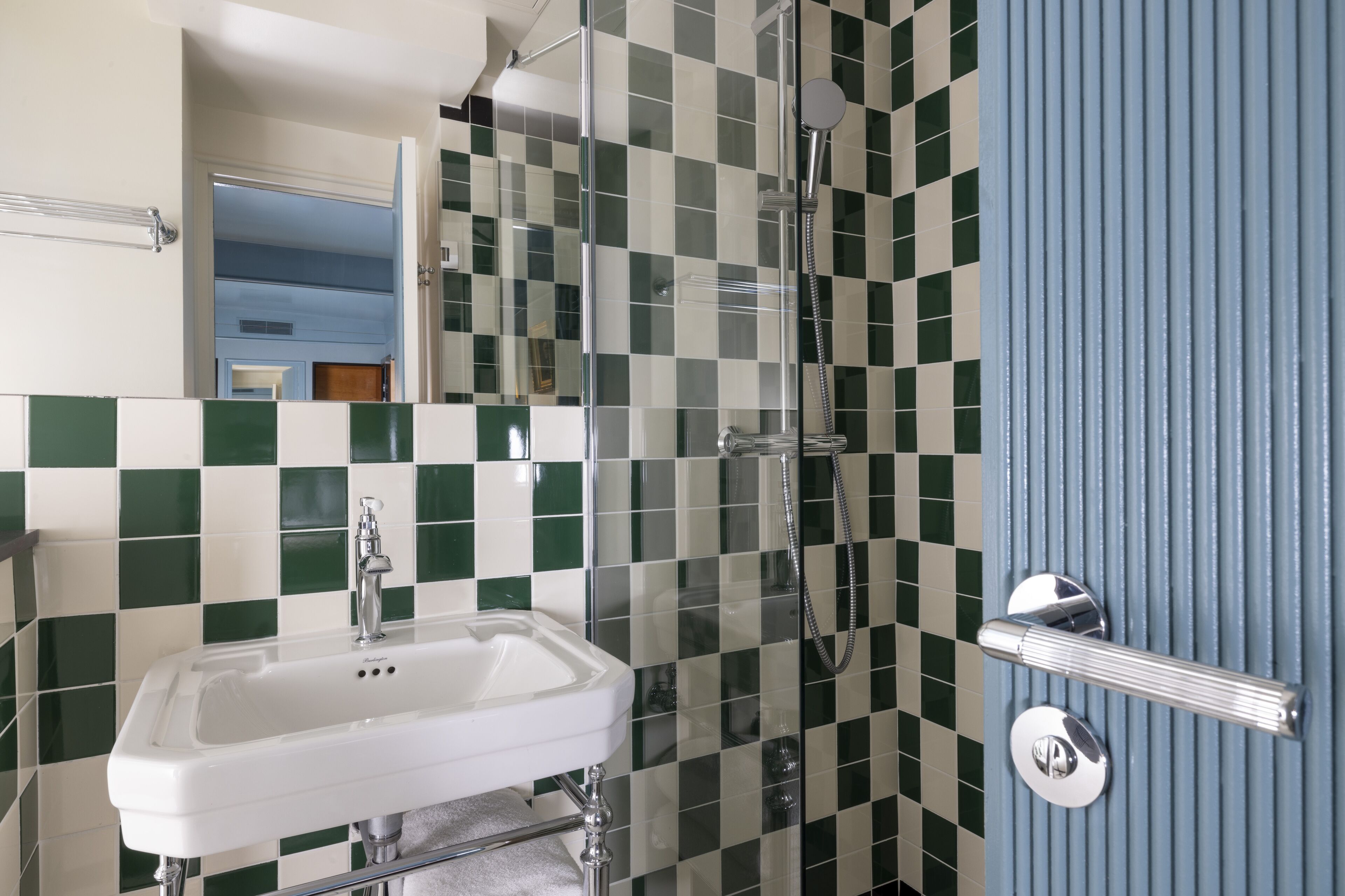 Une salle de bain avec un lavabo blanc, une cabine de douche en verre et une porte bleue.