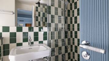 Une salle de bain avec un lavabo blanc, une cabine de douche en verre et une porte bleue.