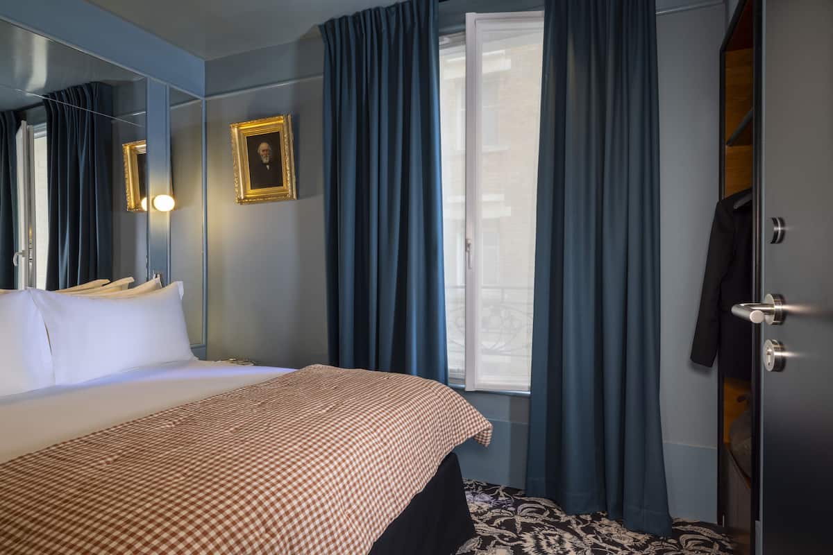 A hotel room with a bed, a mirror, a framed picture, and a wardrobe.