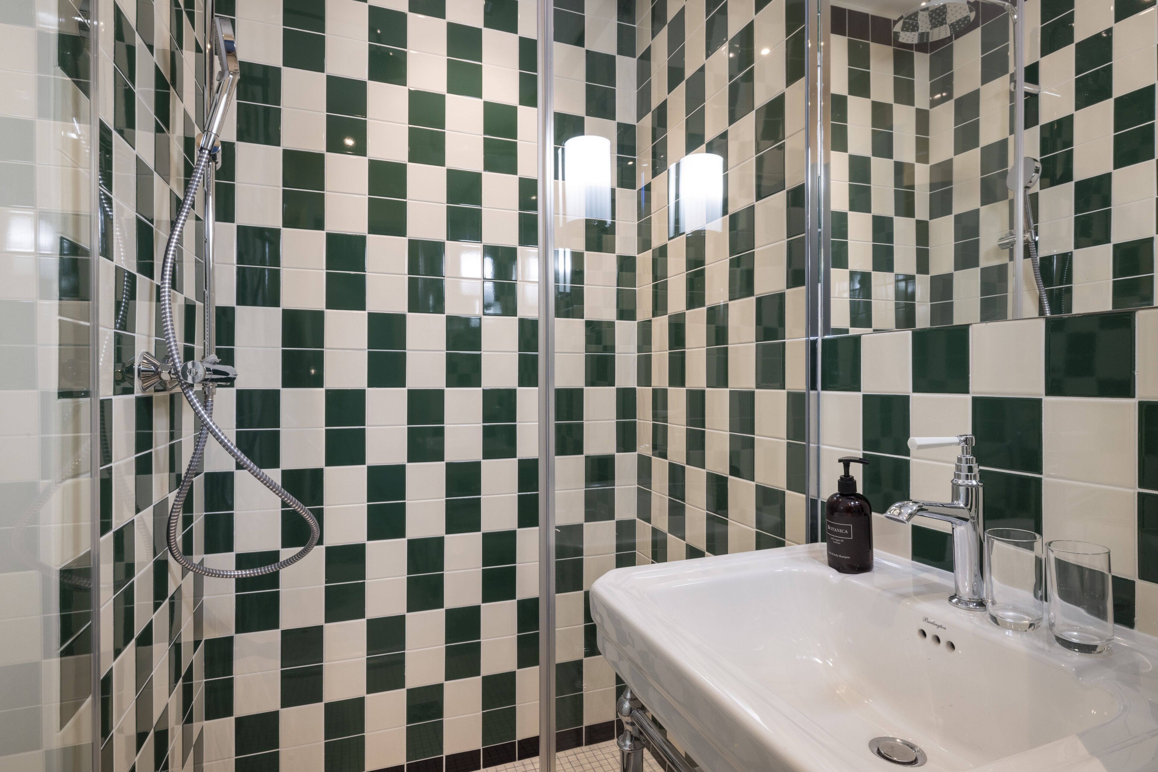 Een badkamer met een betegelde muur in ruitpatroon, een wastafel en een spiegel.