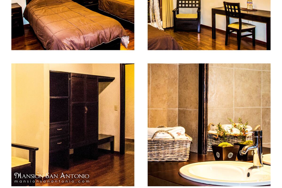 A hotel room with a bed, a desk, a chair, and a bathroom with a sink and mirror.