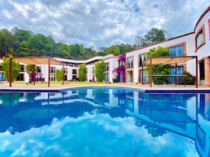 A pool with a reflection of buildings and trees, surrounded by a landscaped area with benches and potted plants.