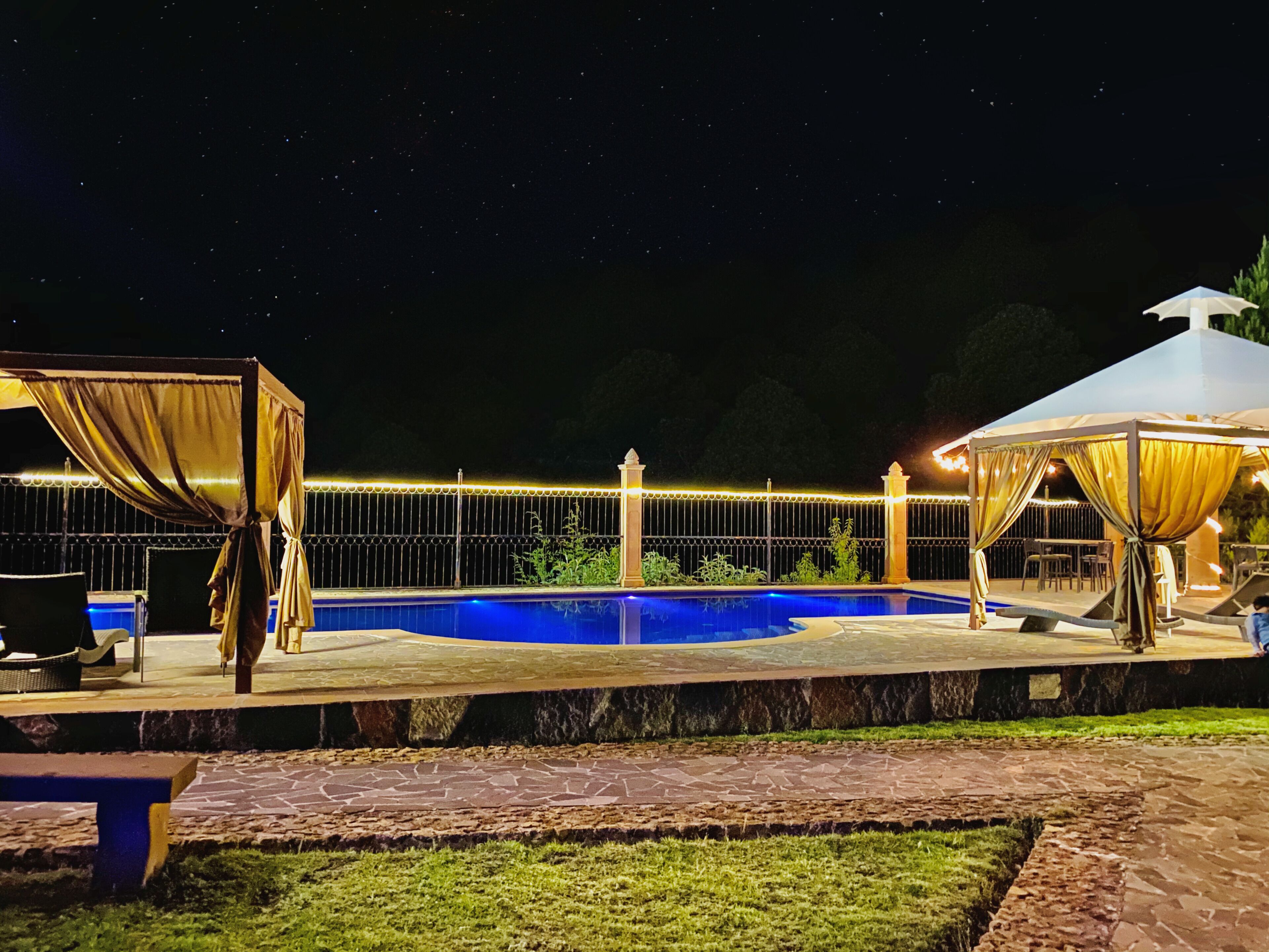 A nighttime outdoor pool area with a covered seating area and a canopy.