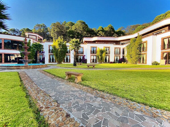 A courtyard with a stone pathway, a fountain, and a pool. - Hotel and Suites Mansion San Antonio (Tlalpujahua)
