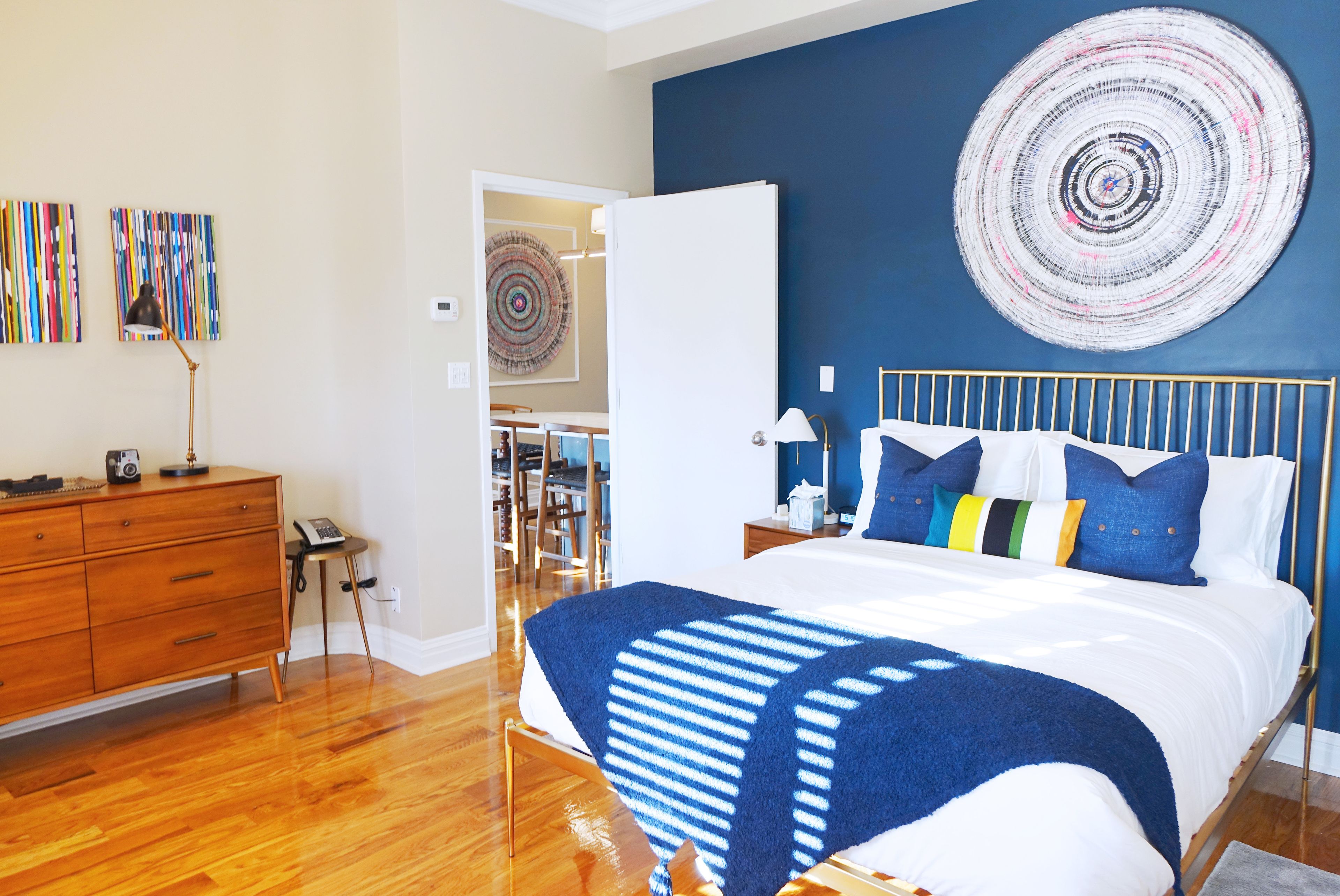 A bedroom with a bed, wooden dresser, and a wall with a circular artwork.