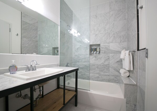 A modern bathroom with a marble wall, a glass-enclosed shower, and a wooden vanity with a sink.