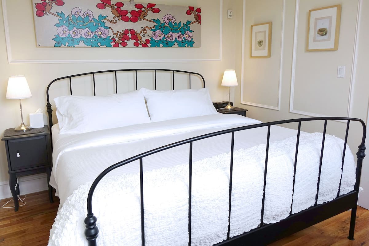 A neatly made bed with white linens, two bedside tables with lamps, and a floral artwork above the bed.