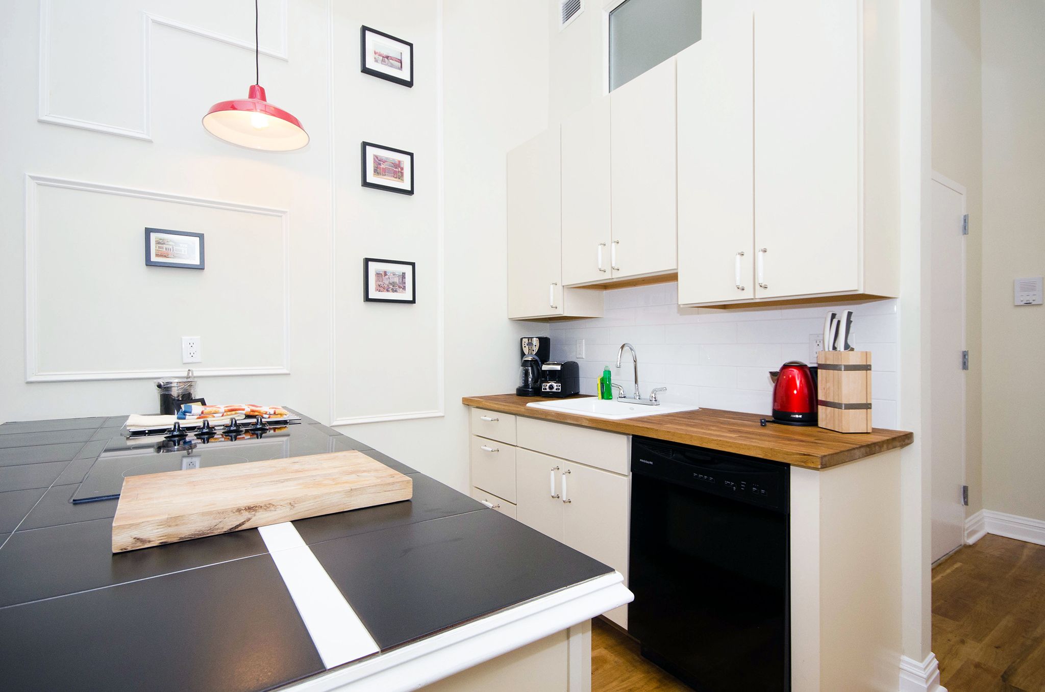 A modern kitchen with white cabinets, a black countertop, and a red kettle.