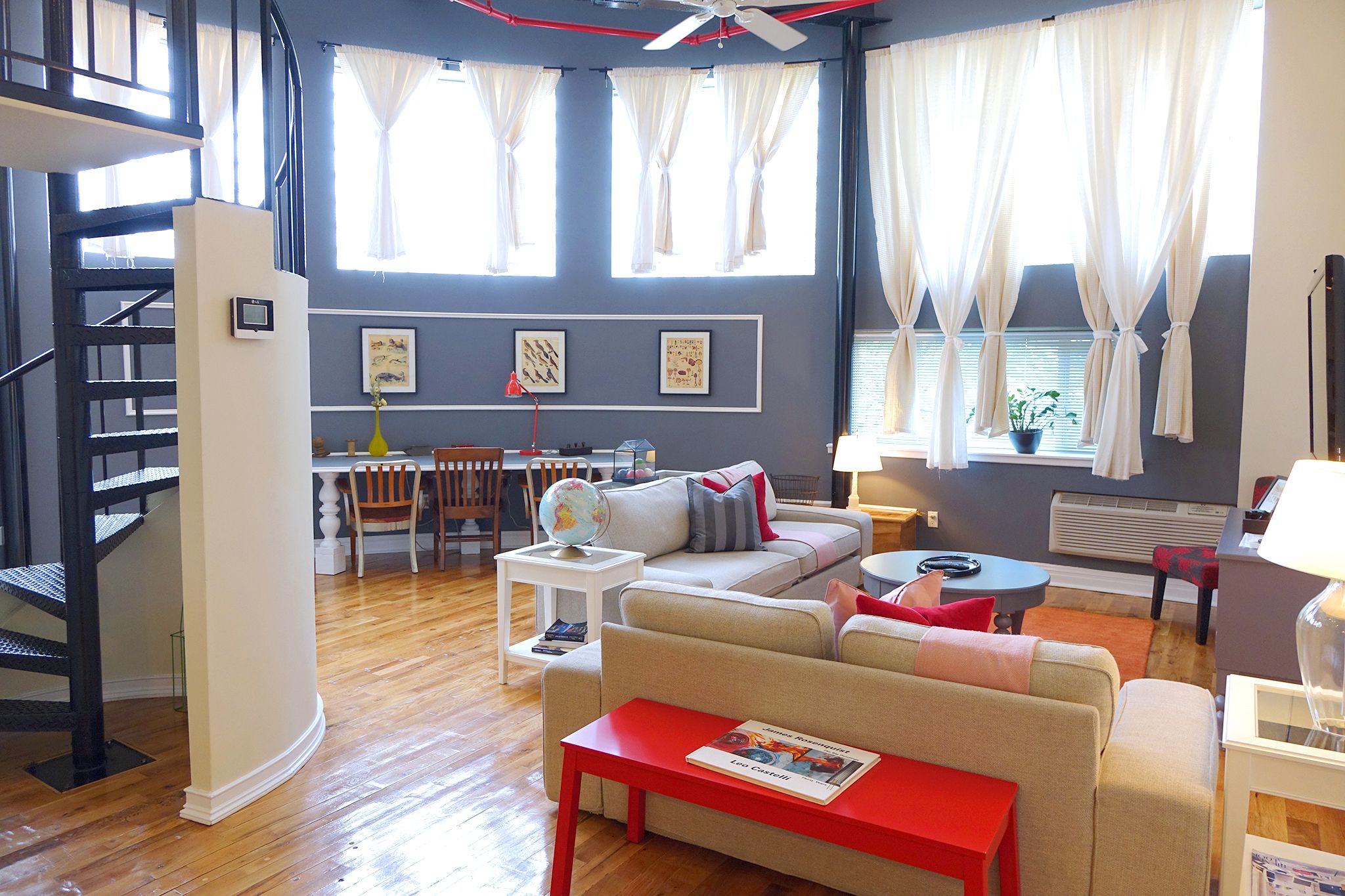 Un saló modern amb escala, zona de menjador i una finestra gran amb cortines.