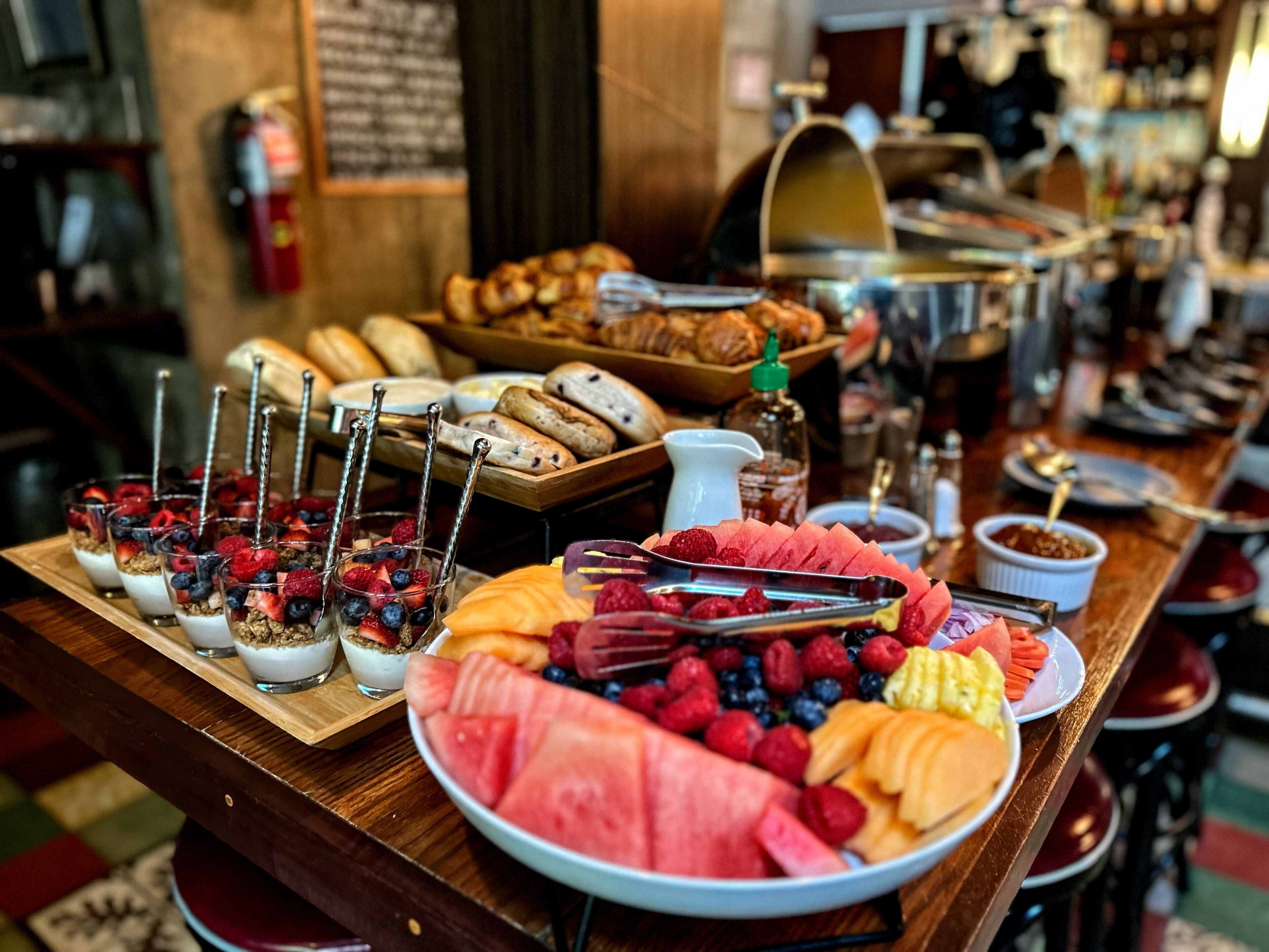 A breakfast buffet with various fruits, pastries, and a coffee station.