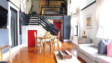 Um apartamento moderno com piso de madeira, área de refeições com mesa e cadeiras, sofá e escada que leva a um andar superior.