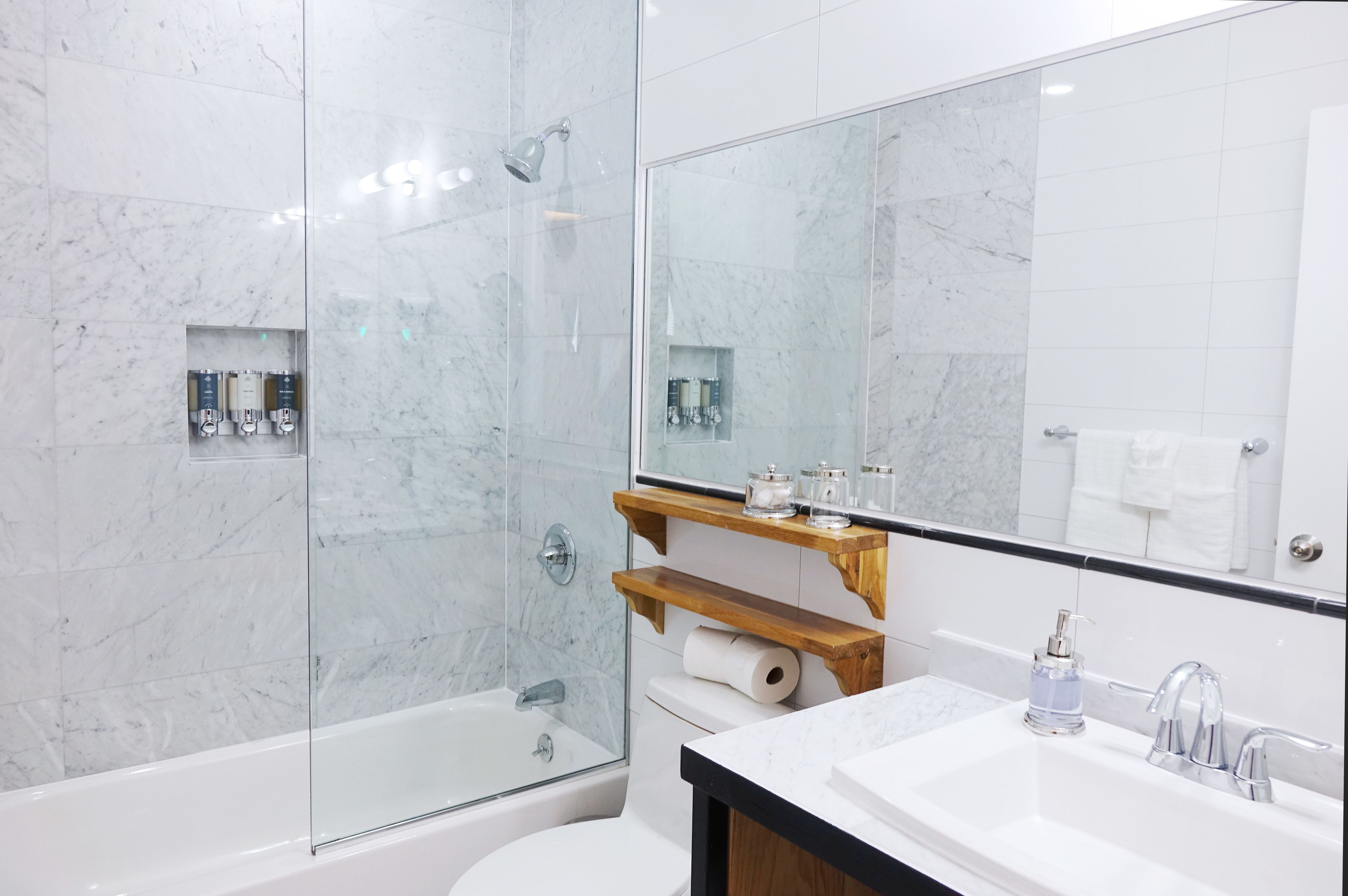 Un baño moderno con ducha envuelta en vidrio, una bañera blanca, inodoro y lavamanos con repisa de madera arriba.