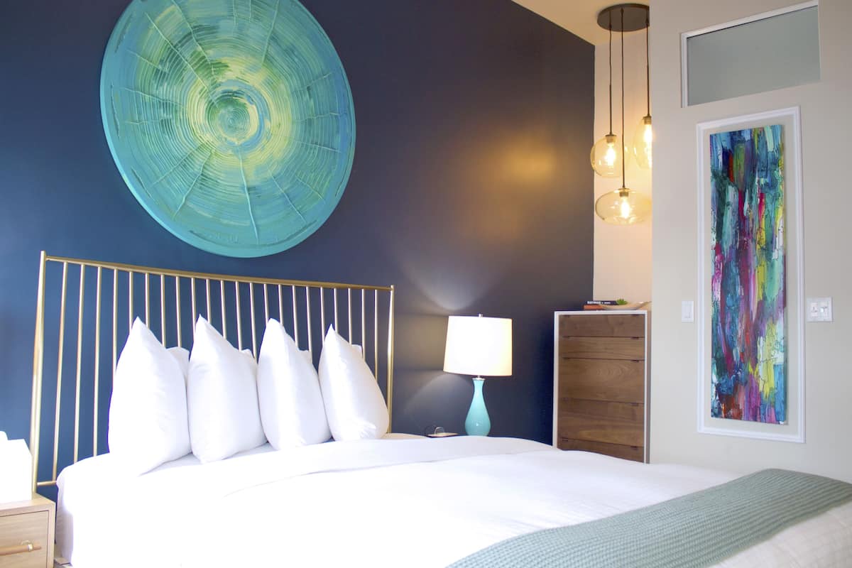 A modern bedroom with a large bed, a circular wall decoration, a dresser, and a colorful abstract painting.
