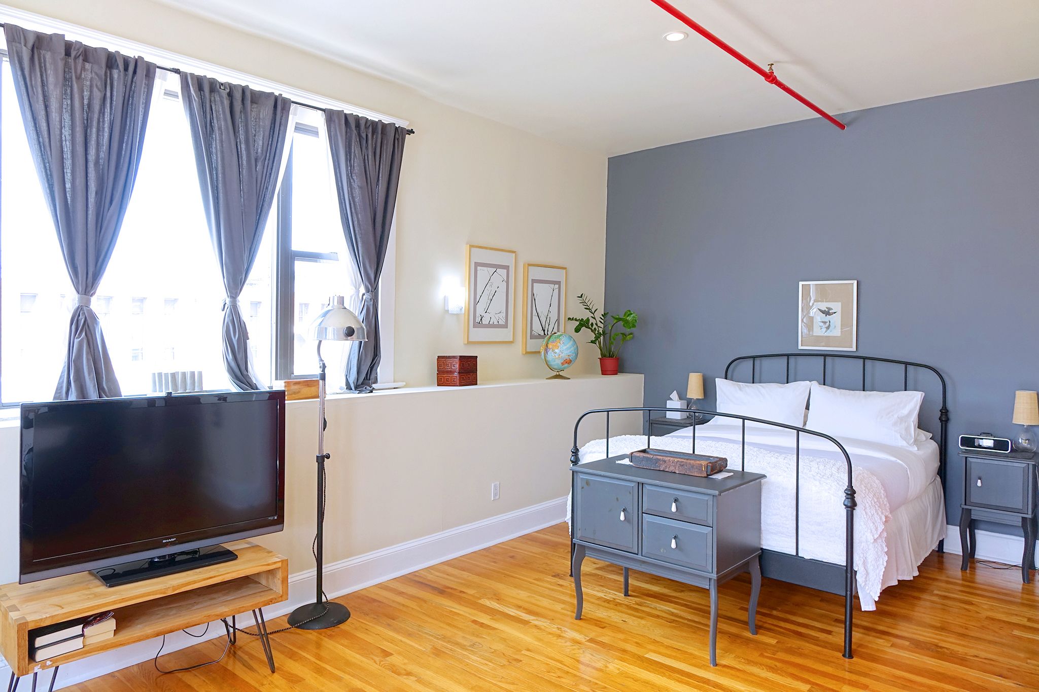 A bedroom with a bed, bedside tables, a TV on a wooden stand, and a window with curtains.