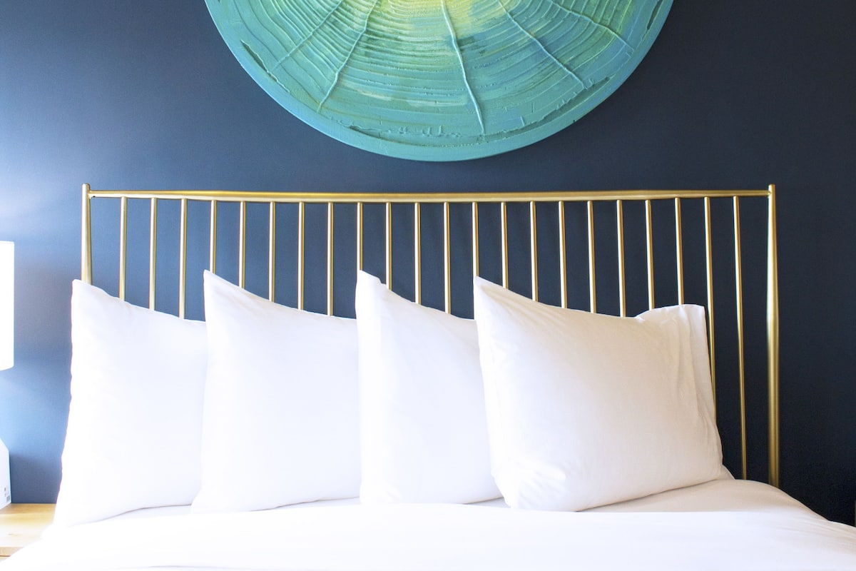 A bed with white linens and pillows, a gold metal headboard, and a circular wall art piece above.