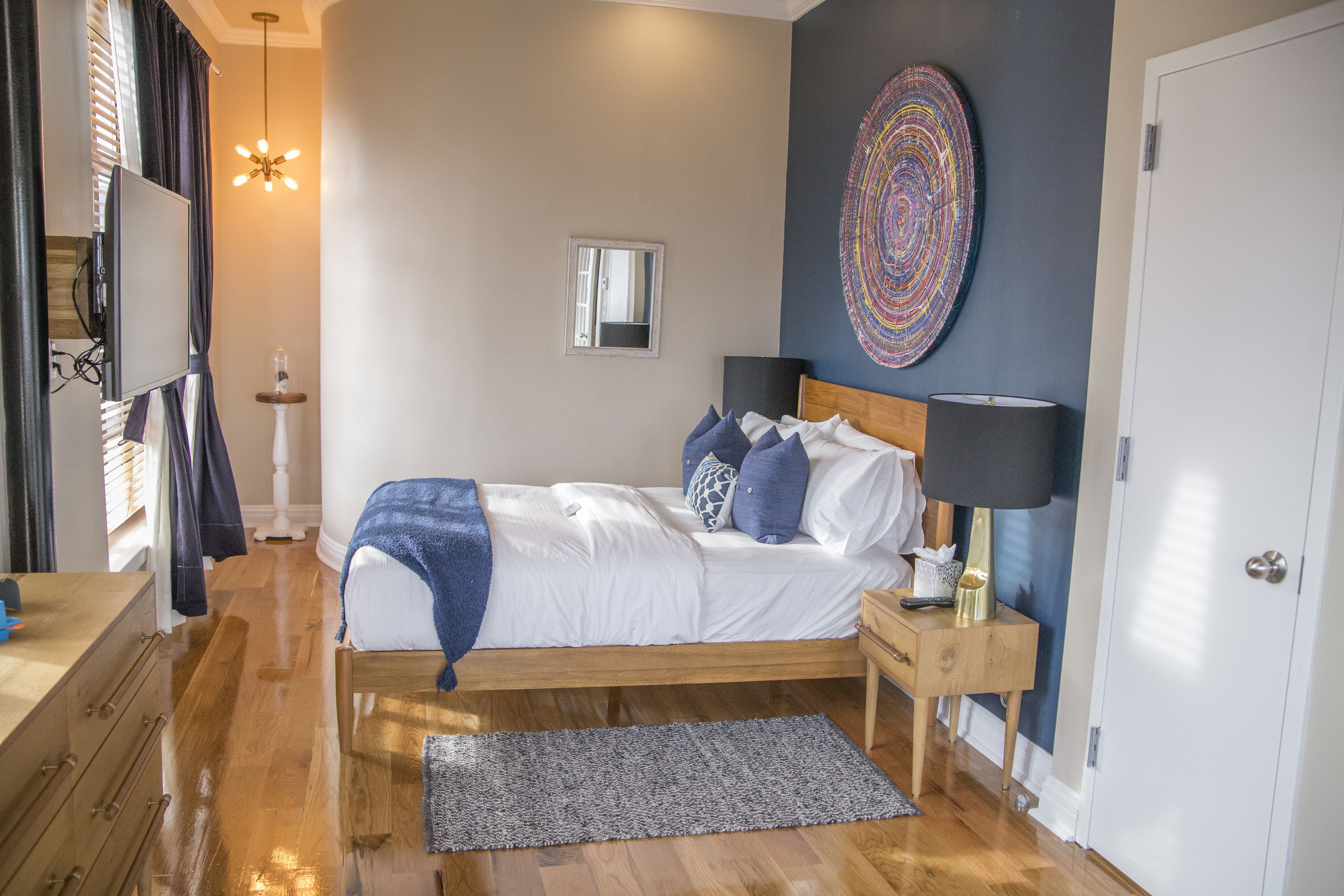 A bedroom with a wooden bed, a bedside table with a lamp, a mirror, and a wall art piece.