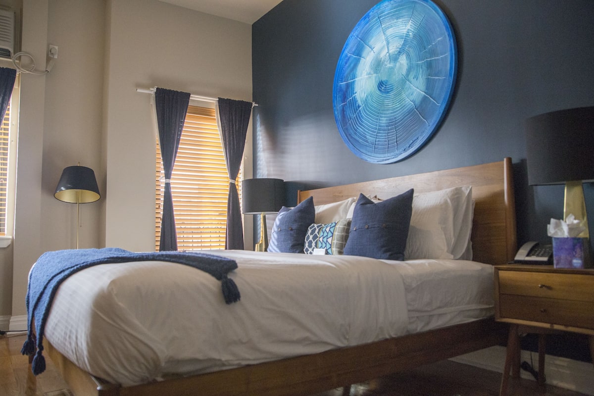 A bedroom with a bed, bedside tables, a wall clock, and a window with curtains.