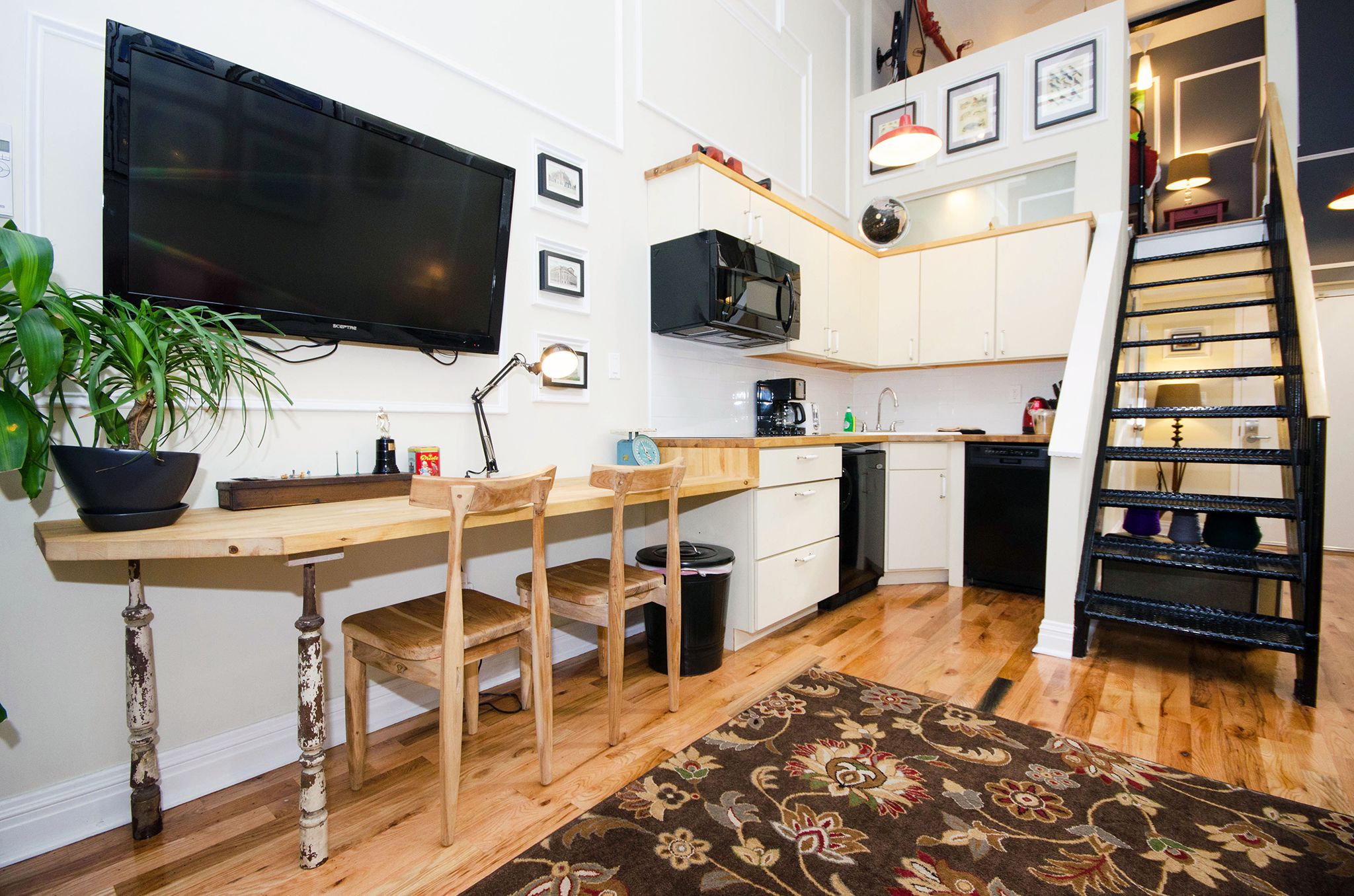 Cocina compacta con televisión de pantalla plana, mesa de comedor de madera y sillas.
