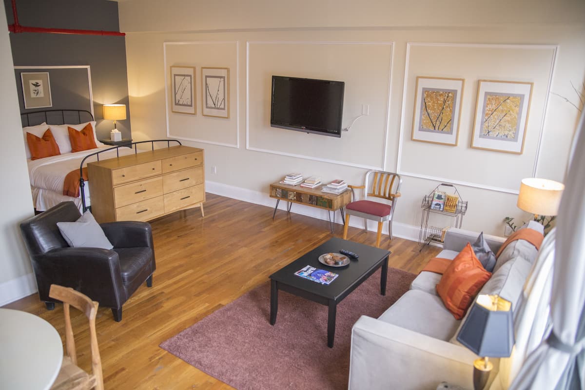A modern living room with a sofa, armchair, coffee table, and a TV mounted on the wall.