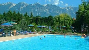 A swimming pool with people swimming and sunbathing, surrounded by trees and mountains in the background. - Miralago (Tremosine)