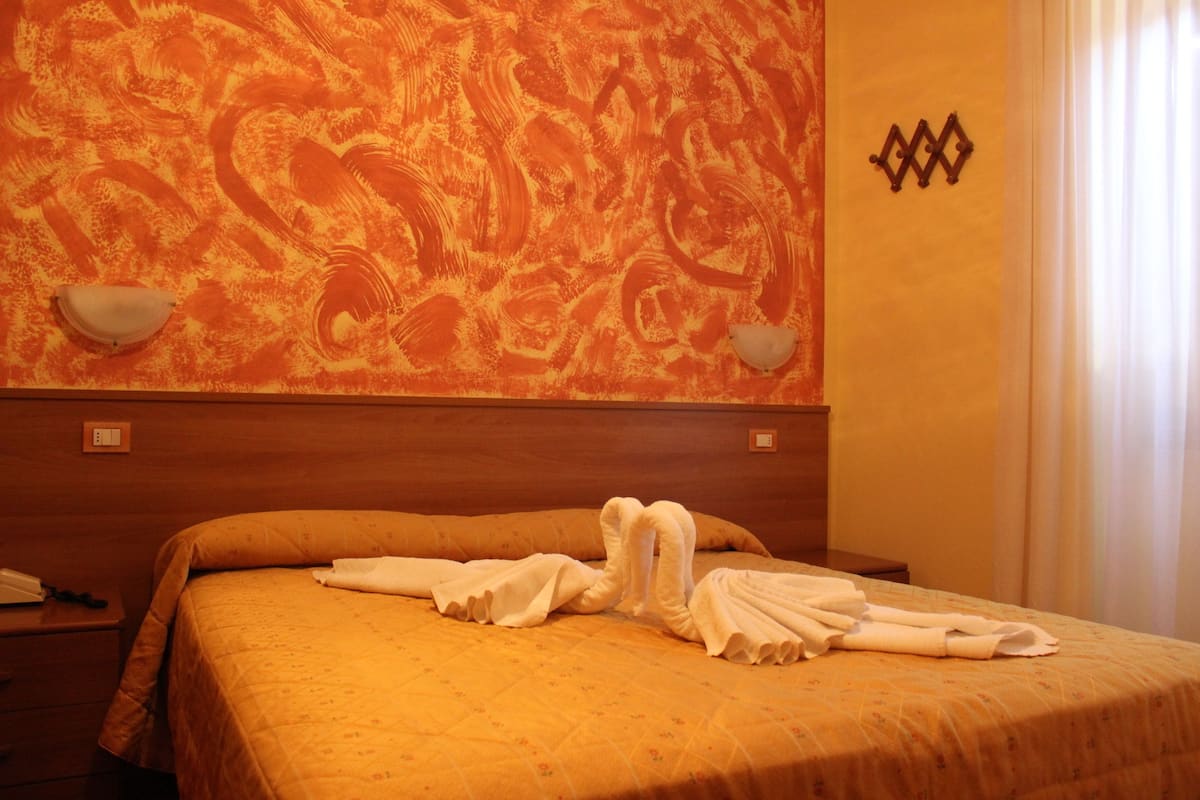 Una habitación de hotel con una cama, un teléfono fijo en la pared y un motivo decorativo en la pared.