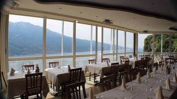 Un restaurante con mesas dispuestas para comer, ventanas amplias que ofrecen vistas a montañas y un lago.